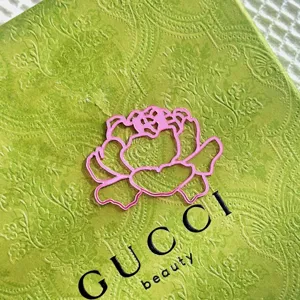 Exquisite pink acrylic flower cake topper presented on a green luxury branded box surface.