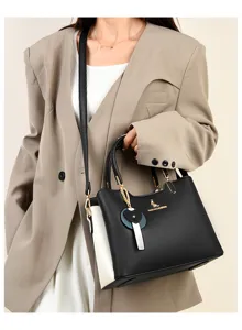 Women's stylish two-tone leather handbag with shoulder strap and chic charm pendant accessory.
