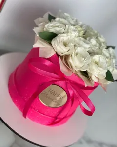 Close-up detail of luxury pink round flower box with white roses and golden birthday tag.