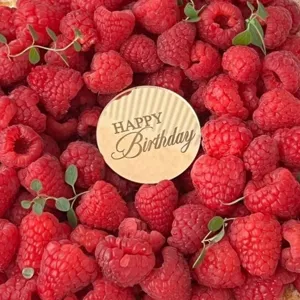 Detail view of gold mirror acrylic happy birthday cake topper surrounded by fresh red raspberries.