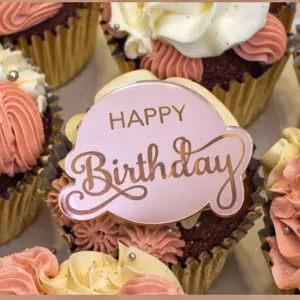 Close-up of pink acrylic round Happy Birthday cake topper with elegant engraved lettering.