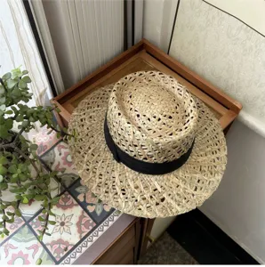 Vista dettagliata del cappello di paglia estivo intrecciato con nastro nero e corona traforata.