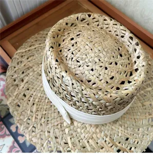 Vista dettagliata del cappello di paglia francese, trama naturale e nastro bianco.