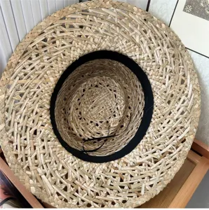 Dettaglio ravvicinato dall'alto del cappello di paglia intrecciata con fascia nera interna.