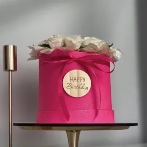 Close up detail of pink round flower gift box featuring white roses and wooden tag