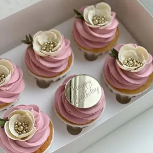 Pink frosting cupcakes with floral decor and Happy Birthday acrylic topper in box