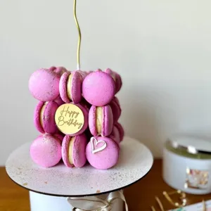 Close-up of pink macaron cube cake decoration with gold happy birthday acrylic disc detail.