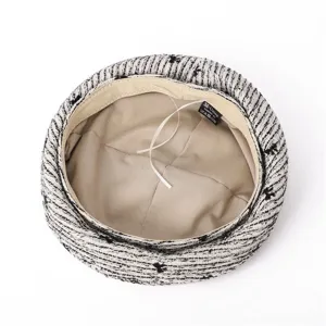 Détail intérieur d'un béret en tweed noir et blanc avec doublure beige et étiquette.