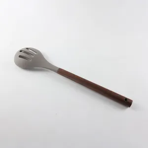 Vue rapprochée détaillée de la cuillère à fentes en silicone gris avec manche en bois.