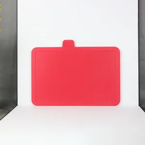 Red plastic cutting board detail view, textured surface with hanging tab for kitchen use.