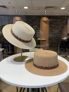 Vista en detalle de sombreros de paja planos con cinturón de cuero de leopardo en mesa.