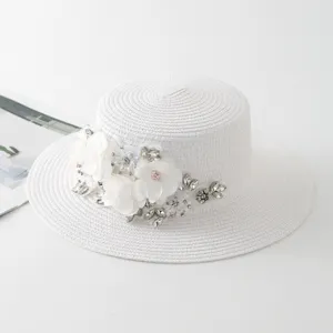 Weißer Strohhut im Detail, flache Form mit eleganten weißen Stoffblumen und feinen Strasssteinen.