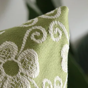 Close up detail of green woven jacquard cushion cover showcasing fine fabric texture and floral pattern.