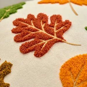 Close-up detail of textured tufted autumn maple leaf embroidery on soft cushion cover fabric.