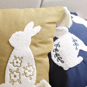 Close-up detail of tufted bunny embroidery pillow cover with tassels, soft textured fabric.