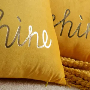 Close-up detail of yellow velvet decorative pillow cover with metallic gold cursive letters.