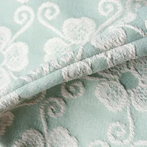 Close-up of mint green clover jacquard fabric showing fine texture and sewing detail.