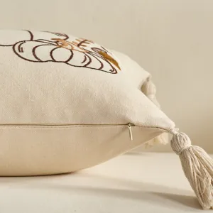 Dettaglio federa cuscino beige autunnale con ricamo di zucca e nappe per divano.