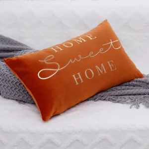 Close-up detail of orange velvet throw pillow cover with gold HOME text, soft texture.