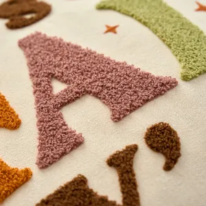 Close-up detail shot of tufted embroidered alphabet cushion cover with autumn theme design.
