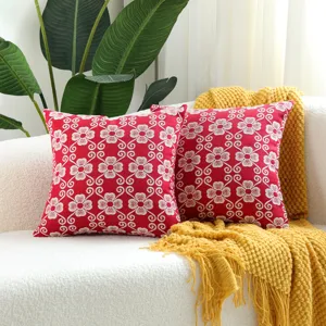 Detail shot of red jacquard throw pillow with white floral pattern on cozy white sofa.