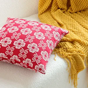 Red and white floral jacquard cushion cover detail showing intricate woven texture and cozy sofa setting.
