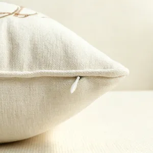 Primo piano di una federa beige con cerniera nascosta e raffinata lavorazione di ricamo.