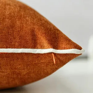 Primo piano di fodera per cuscino in velluto arancione con profilo bianco e zip.
