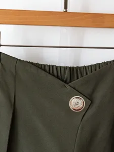 Close-up view of the dark green trousers featuring an asymmetrical waist and ornate golden button.