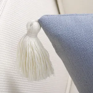 Close-up detail of blue textured cushion cover corner with white tassel. Fine quality fabric.