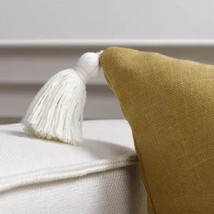 Close-up detail of mustard yellow throw pillow cover with white tassel, soft home decor fabric