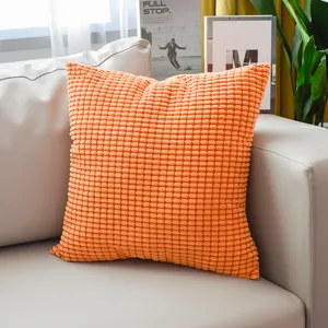 Modern orange corduroy throw pillow with textured corn kernel design on a clean white sofa.