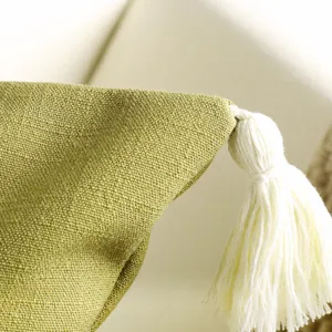 Close-up of green textured fabric cushion cover featuring a delicate white tassel trim.