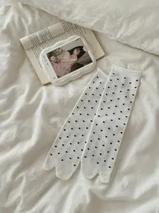 Detail view of women's white split toe mid calf socks with black polka dots for trendy shoes.