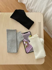 Flat lay detail of thin solid color knit leg warmers in black grey and off-white.