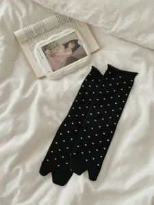 Close-up detail of black split-toe socks featuring white polka dots on soft white bed sheet.