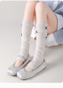 Detail view of white knitted leg warmers with cute black bows and breathable mesh design.