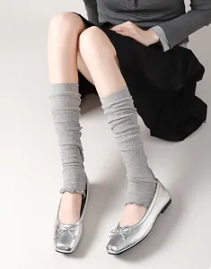Nahaufnahme von grauen Strick-Beinstulpen mit Rautenmuster zu eleganten silbernen Ballerinas.