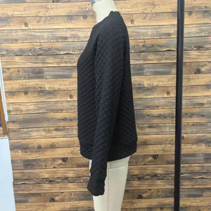 Detailed side close-up view of women's black quilted textured long sleeve top.