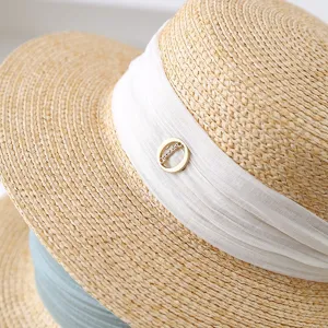Close-up detail of summer straw hat with elegant white ribbon and gold metal charm accent.