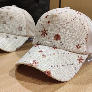 Dettaglio ravvicinato del berretto da baseball in tweed beige con paillettes, rete e motivi floreali.