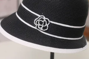 Cappello da sole in paglia nero e bianco con dettaglio di camelia di perline per estate.