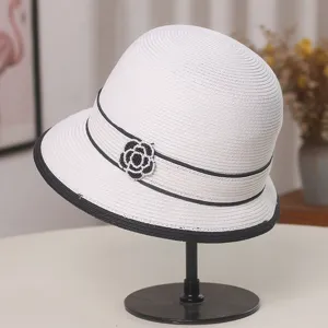 Elegante cappello a secchiello in paglia bianca da donna con nastro nero e fiore di camelia.