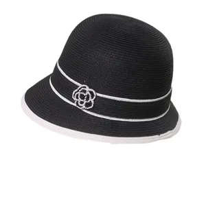 Cappello di paglia nero da donna con nastro bianco ed elegante decorazione di camelia estiva.