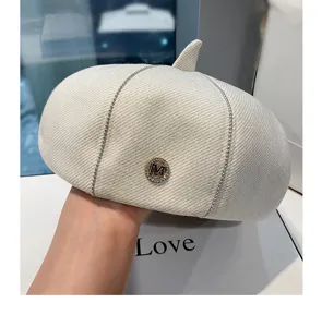 Dettaglio berretto bianco con logo lettera M in strass e delicata decorazione a catena.