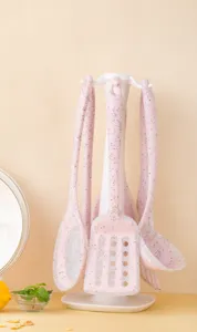 Pink speckled silicone kitchen utensil set detail with white hanging rack on table.