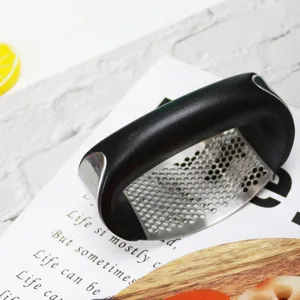 Stainless steel garlic press detail view, ergonomic black handle, kitchen gadget close up.