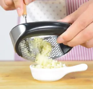 Detail view of manual stainless steel curved garlic press squeezing fresh minced garlic.