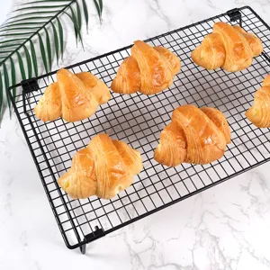 Black wire cooling rack for baking bread and cakes, placed on tabletop with fresh croissants.