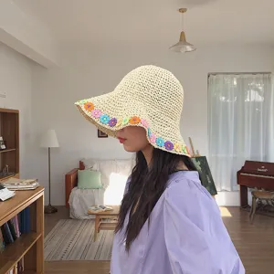 Dettaglio del cappello da sole in paglia beige con decorazioni floreali colorate.